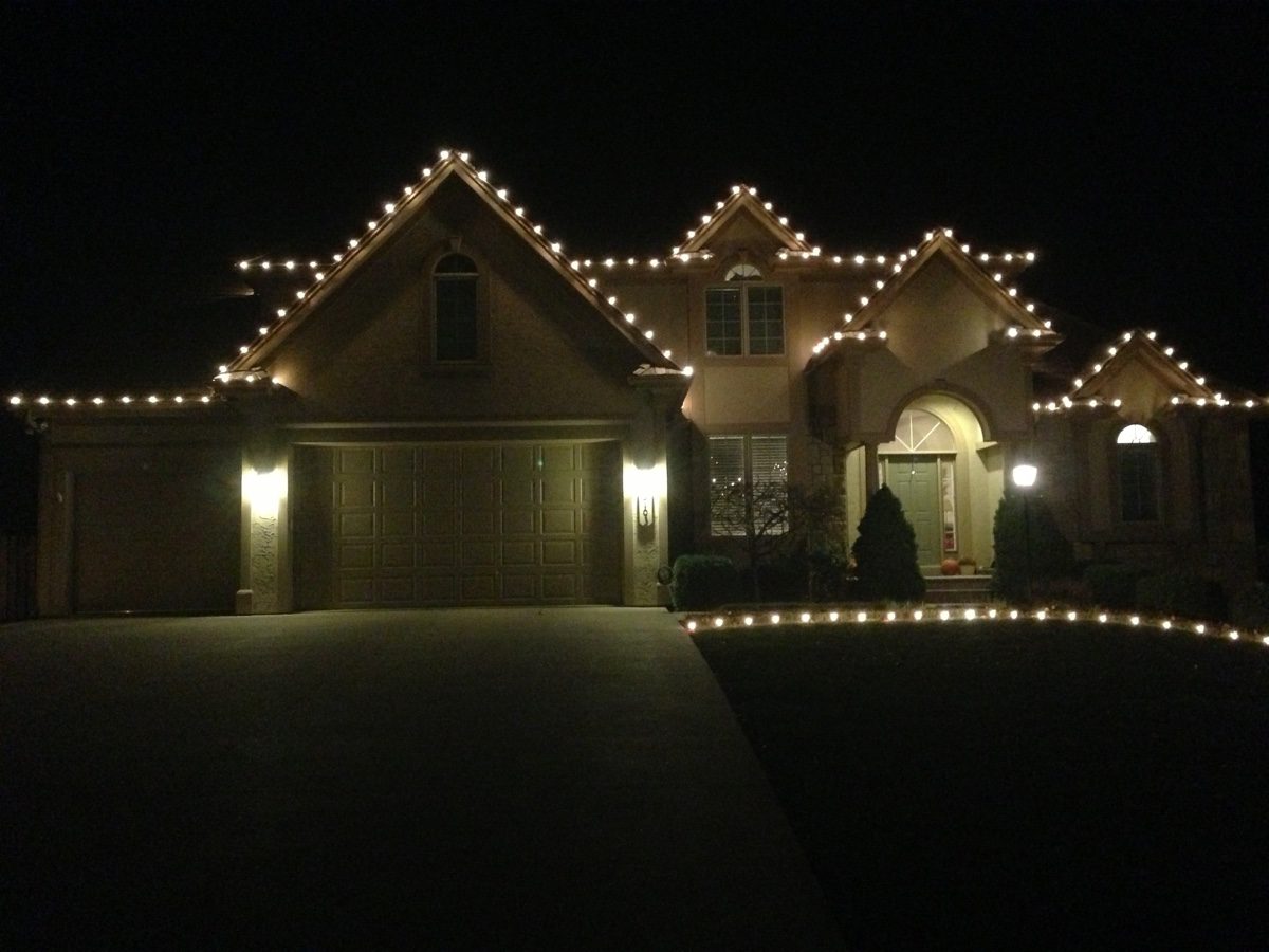 A stucco home with warm white bulbs on every gable and a line of lights edging the front lawn